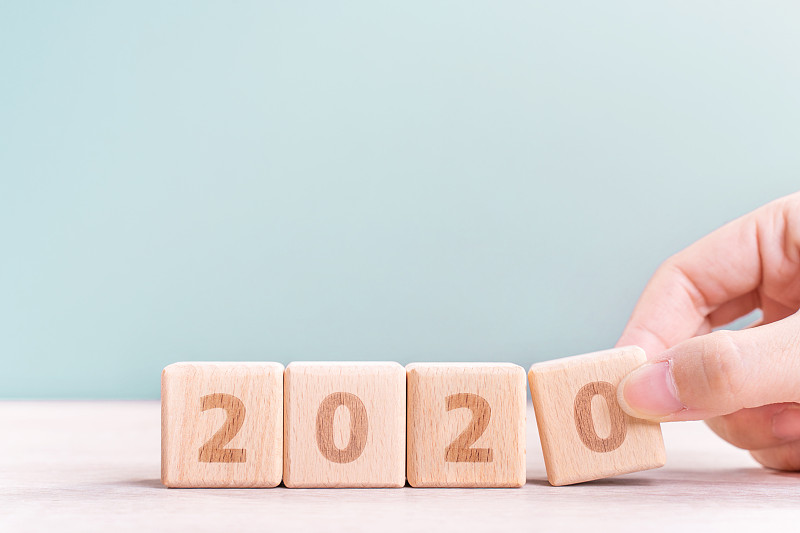 2020年& 2019年新年倒计时设计理念——女子手持木桌、绿色背景的木块立方体。