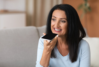 成熟的女人在智能手机上使用语音助手