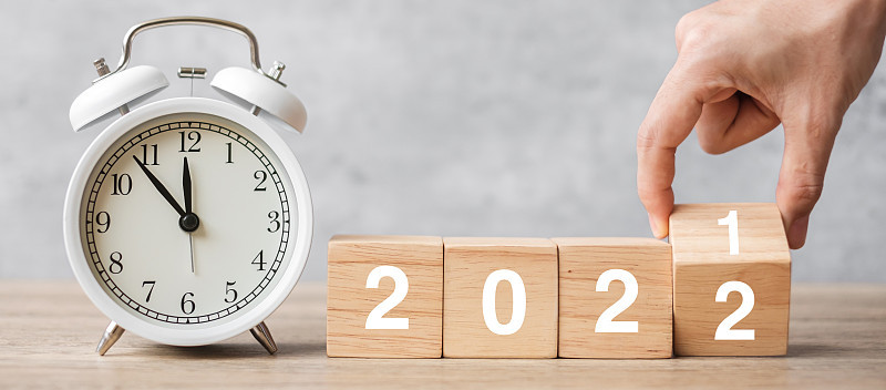 新年快乐，老式闹钟和手翻转2021年改为2022块。圣诞节，新的开始，决心，倒计时，目标，计划，行动