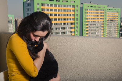 一个带着黑猫的女孩从阳台看向一座新楼