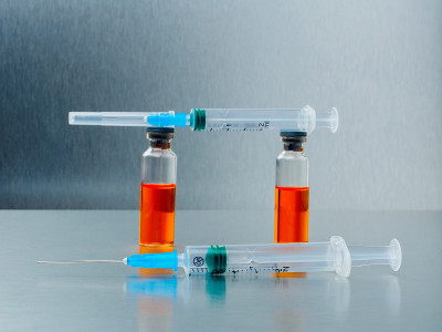 特写注射注射器和安瓿与橙色冠状病毒疫苗在银色铝背景。