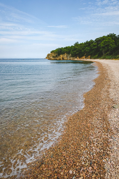 夏日蔚蓝清澈的大海全景。浅浅的透明的海洋，周围有珊瑚礁、岩石和绿色的小山。日本海洋。俄罗斯的滨海边疆