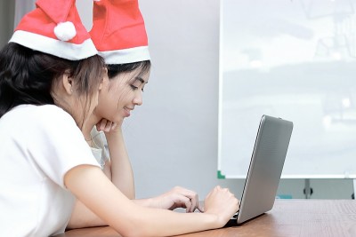 年轻的亚洲女性戴着圣诞老人的帽子，在家里的客厅里用笔记本电脑在网上购物。圣诞快乐，节日快乐的概念。