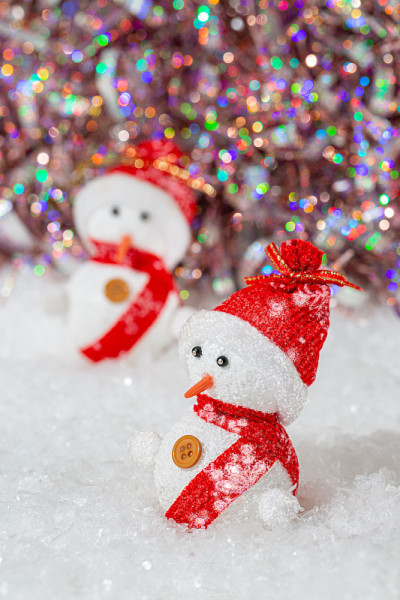 圣诞装饰。雪人戴着红帽子和围巾。雪人在洁白的雪堆旁边有一个七彩闪闪的散景背景。