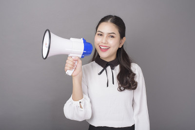 美丽的亚洲女人拿着扩音器在灰色背景的工作室