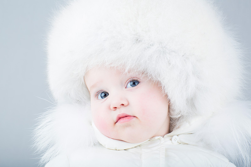 滑稽的婴儿穿着白色的雪衣和大皮帽