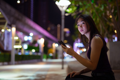 美丽的亚洲女人晚上在户外使用手机