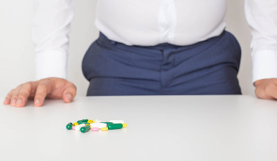 A handful of pills lie on the table, with a man st