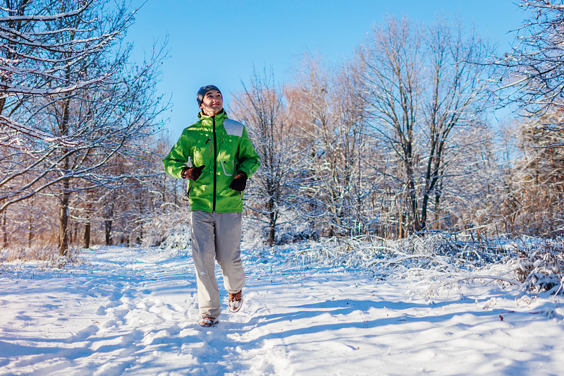 跑步运动员在冬季森林里冲刺。在寒冷的下雪天进行户外训练。积极健康的生活方式