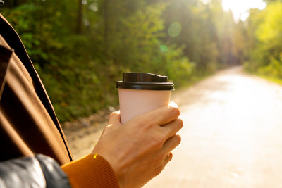 Young woman holds a disposable cup of coffee on on