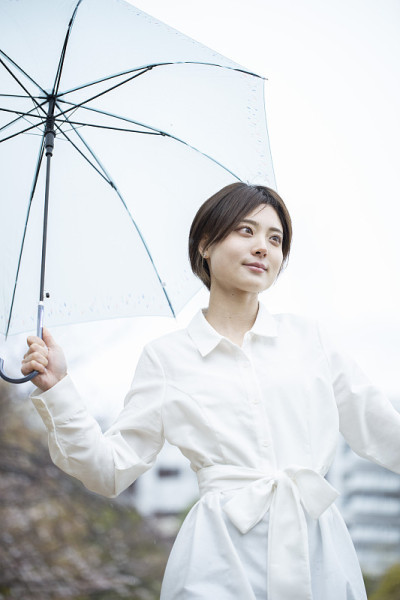 一个穿着白色连衣裙的年轻女子撑着伞在雨中行走