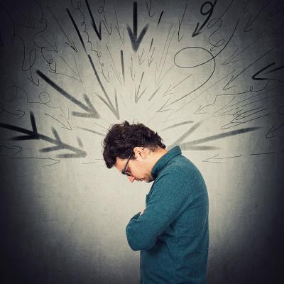 心烦内敛的人向下看很烦恼，感到沮丧。孤独的男人经历情感危机。一个人在工作中受到压力，墙上有多个箭头指