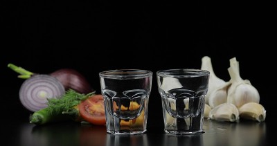 用小酒杯喝伏特加。背景用蔬菜