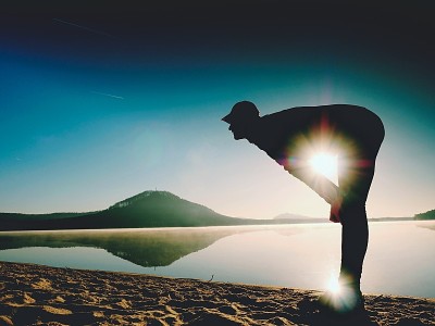 男人在海滩上锻炼。活跃男子在湖边锻炼和伸展的剪影