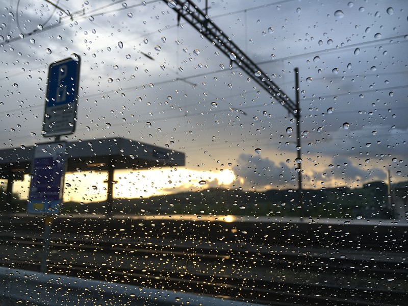 汽车玻璃上的雨滴与日落和背景中的火车站失去了焦点-圣加仑，瑞士