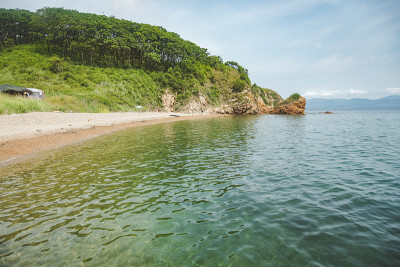 夏日蔚蓝清澈的大海全景。浅浅的透明的海洋，周围有珊瑚礁、岩石和绿色的小山。日本海洋。俄罗斯的滨海边疆