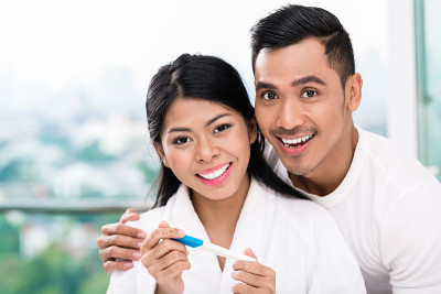 一对亚洲夫妇在床上拿着验孕棒