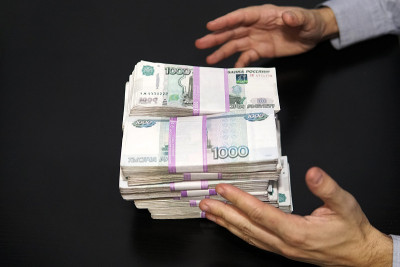 男人的手伸向一叠钱。一百万卢布放在黑色的桌子上。财富和成功的概念。