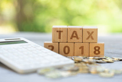 单词块“TAX”，以及以计算器为背景的一堆硬币上的“2018”。收入，费用，税收，财务数据。