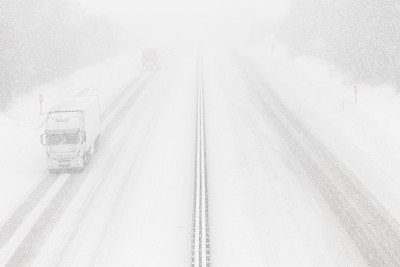 高速公路上的大雪。危险的冬季天气，能见度低。白色货车在高速公路上
