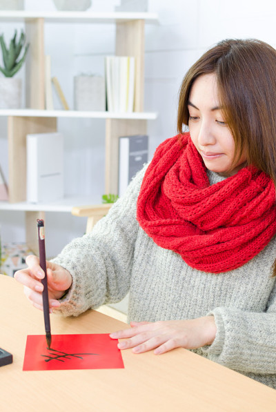 年轻的亚洲妇女用中国书法毛笔和砚台写春联。春节时在门上贴春联是中国文化的传统。