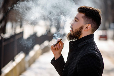 一幅穿着黑色外套、蓄着胡须、英俊潇洒的年轻男子在外面抽烟的肖像。