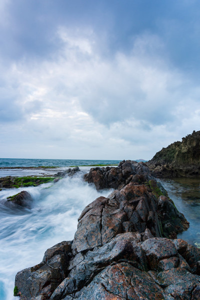 在雨季，海岸上有波浪和青苔的沉积岩海滩