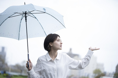 一个穿着白色连衣裙的年轻女子撑着伞在雨中行走