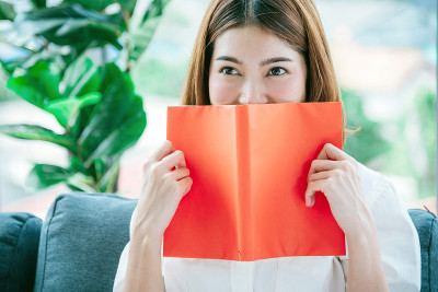 放松的亚洲女人读书坐在客厅的沙发上抱着书读。18、少妇舒心读书，读书开卷休闲心灵。幸福美女人笑脸幸福