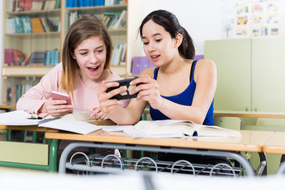 年轻女孩正在教室里谈论拿着手机的男孩