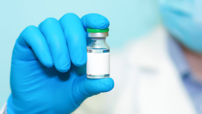 戴蓝手套的医生拿着一个装有疫苗的瓶子。医学、保健和科学的概念