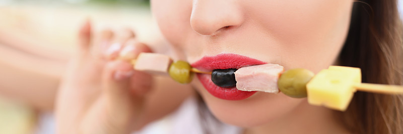 一个女人吃着烤肉串上的橄榄和火腿