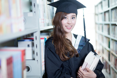 亚洲女学生拿着书，穿着学术服装