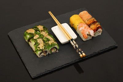 日本料理餐厅，寿司卷盘或拼盘套装。复制空间，筷子，生姜，酱油，芥末。寿司放在黑石头上。前视图。
