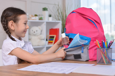 一个女生把洗手液和口罩放进背包里。2019冠状病毒病大流行后的学生安全。新冠肺炎疫情爆发后回到学校。