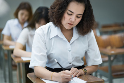 选择性焦点的青少年大学生坐在讲座椅上做期末考试和写在试卷上的答题卡在教室里。大学生在教室里穿制服。