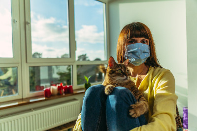 医学的面具。一个女人戴着医用口罩，怀里抱着一只猫。