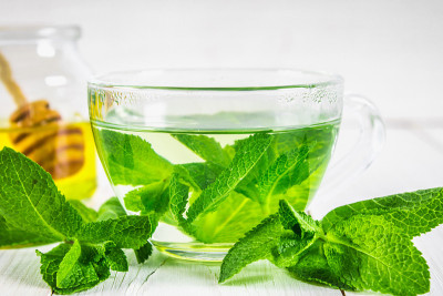 薄荷茶装在杯子里，蜂蜜罐放在白色木桌上。