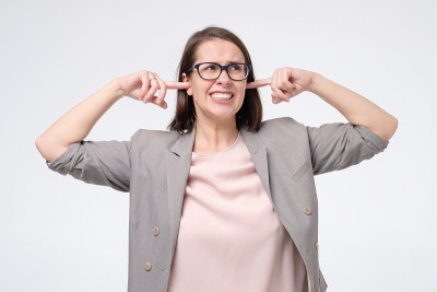 成熟的女人戴着眼镜，有不满的表情，堵着她的耳朵，被噪音惹恼
