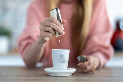 一个女人把糖精药丸扔在家里厨房的咖啡杯上。
