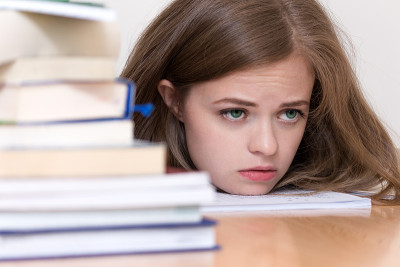 年轻的白人女孩与许多书在学校或大学学习，看起来疲倦，压力或疲惫