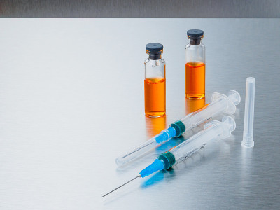 银色铝制背景的橙色冠状病毒疫苗注射器和安瓿。