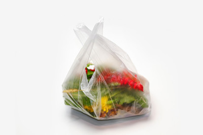 散焦。塑料工厂。红色和绿色的植物花在一个塑料袋在白色的背景。一根干草叶伸出来。生态问题。的焦点