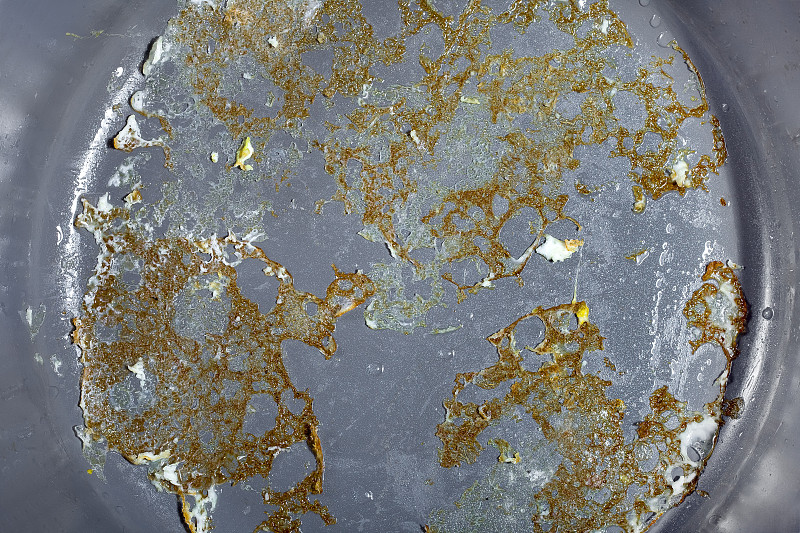 灰色的不粘平底锅表面有烧焦的煎蛋特写，厨房用具用于烹煮油炸食品，无人。
