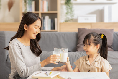 亚洲母亲和她的女儿碰杯享受和微笑的牛奶饮料。妈妈和小女孩拿着牛奶杯喝来补充钙质。健康饮食的概念