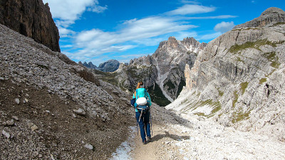 一名女子背着背包，拄着拐杖在意大利Dolomites的一条狭窄小路上徒步旅行。她周围有陡峭的山脉。很