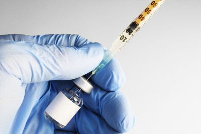 手上带空白标签的小瓶和手套。液体被输送到注射器。