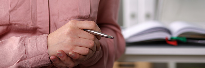Close-up girl in business clothes holds silver pen