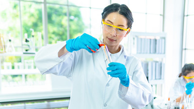 科学家在实验室。女研究员白袍聚精会神地看着测试化学液体。室内以白色为背景的实验室。