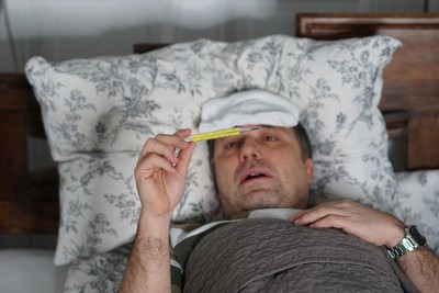 一个又累又病的男人躺在床上检查他的体温